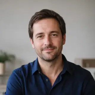 Portrait de Ambroise Marchessault, cheveux bruns courts, barbe naissante, chemise bleu nuit, sourire discret, fond clair flou