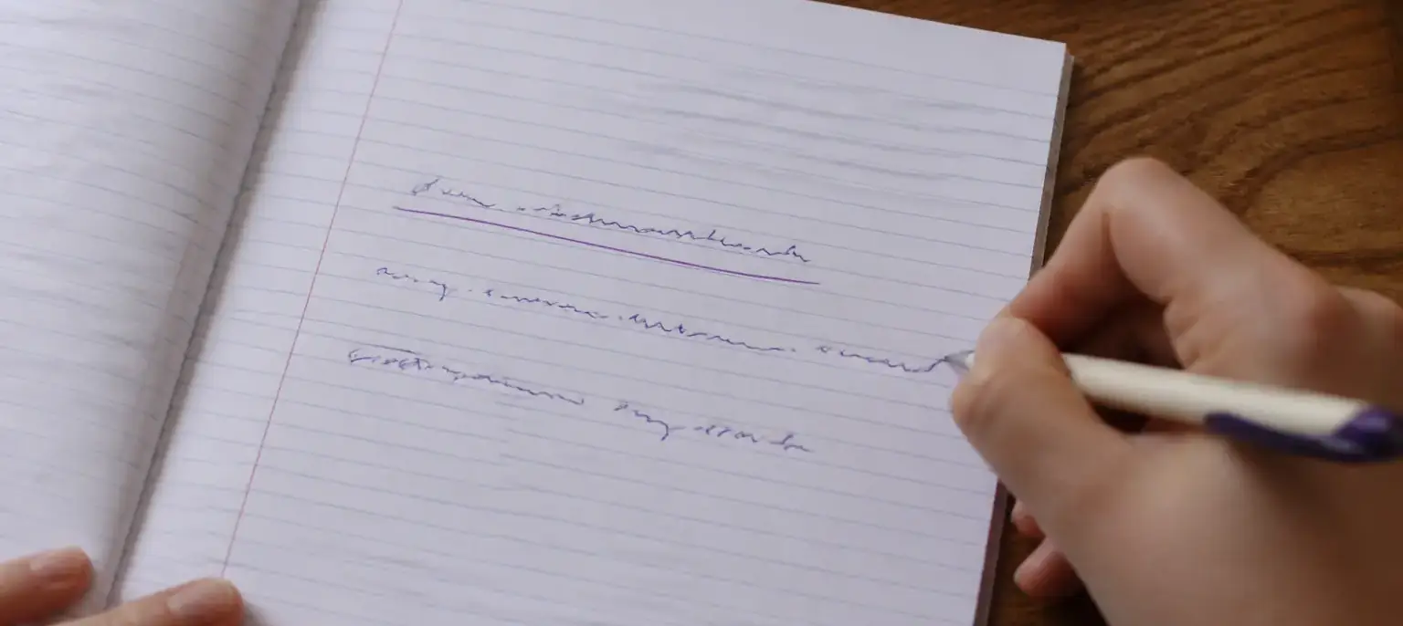 Une feuille de cahier avec trois phrases simples copiées à la main, la première soulignée à l’encre violette