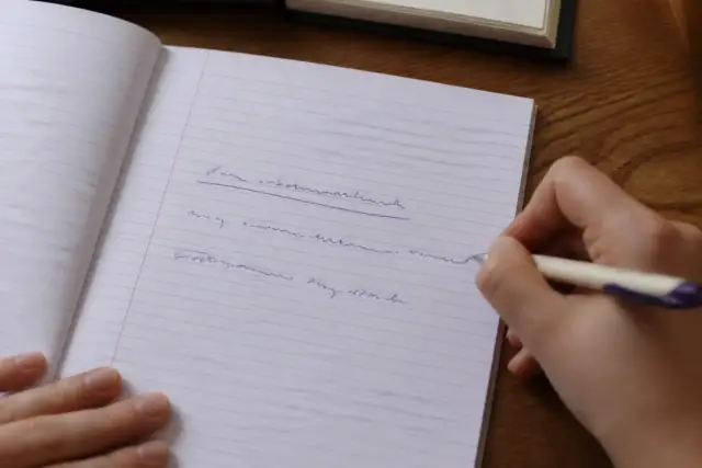 Une feuille de cahier avec trois phrases simples copiées à la main, la première soulignée à l’encre violette