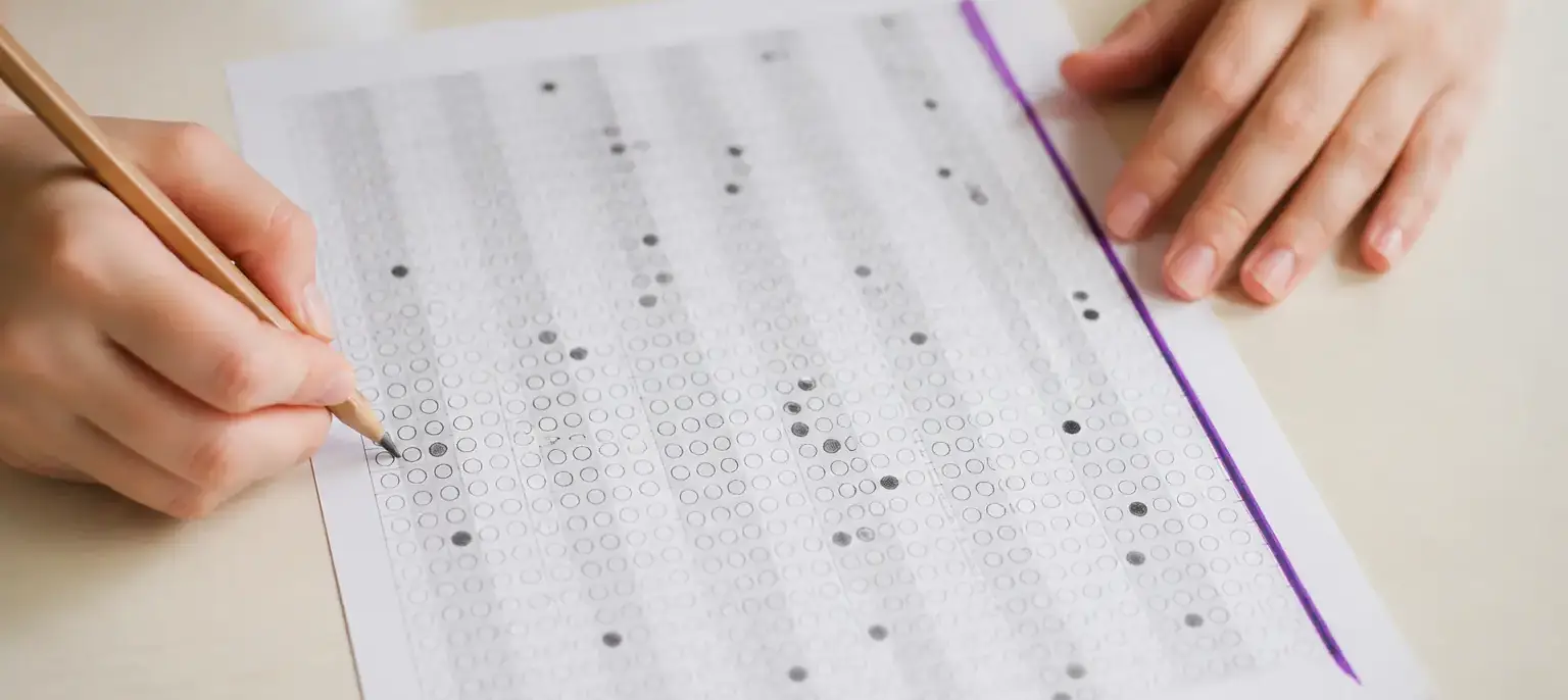 Une grille de réponses cochées au crayon posée sur une table, avec un trait d’encre violette en marge