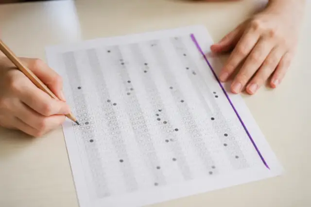 Une grille de réponses cochées au crayon posée sur une table, avec un trait d’encre violette en marge