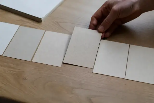 Rangée de petites cartes de papier crème de teintes à peine différentes, alignées sur une table en bois clair, l’une légèrement décalée