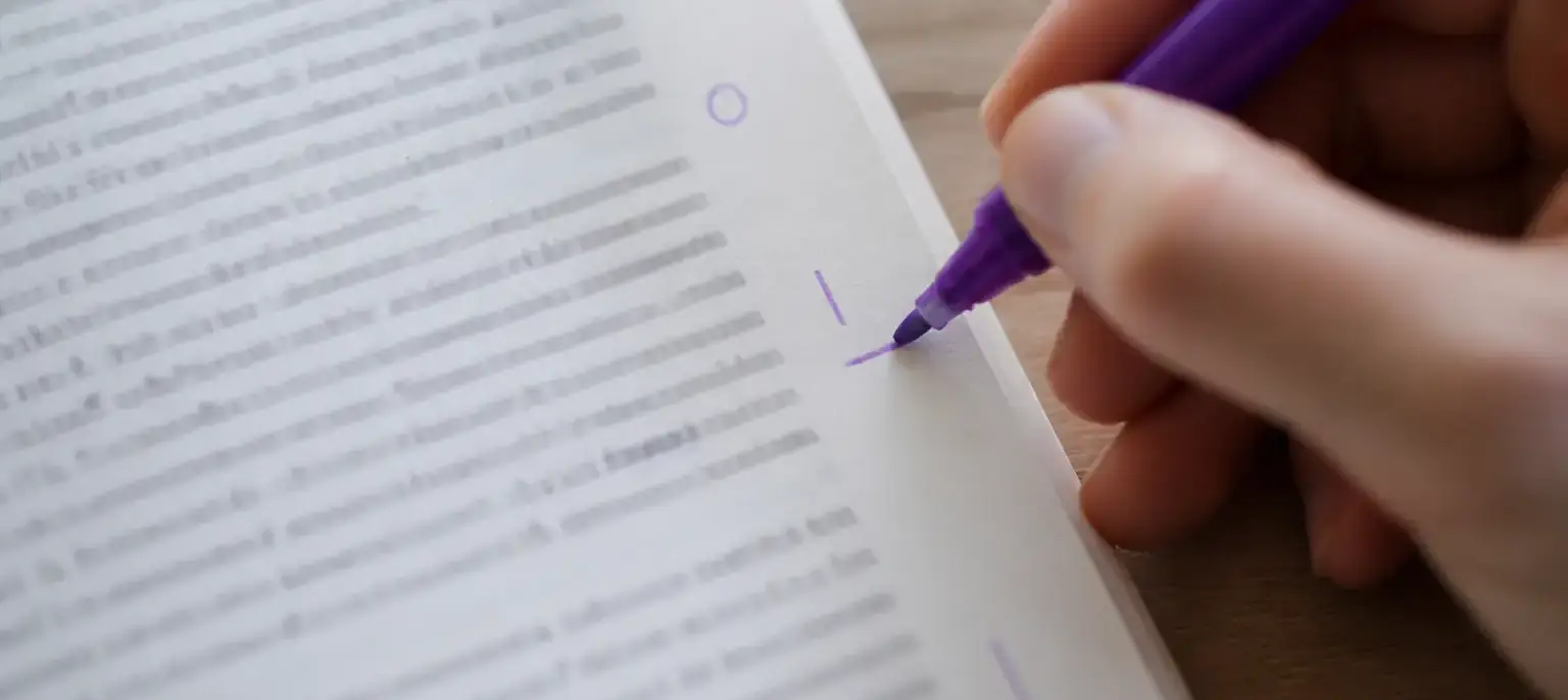 Une main souligne un mot à l’encre violette dans la marge d’une page imprimée