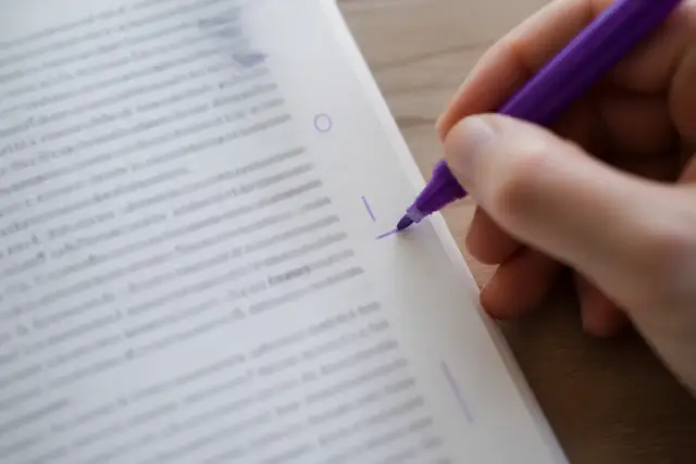 Une main souligne un mot à l’encre violette dans la marge d’une page imprimée