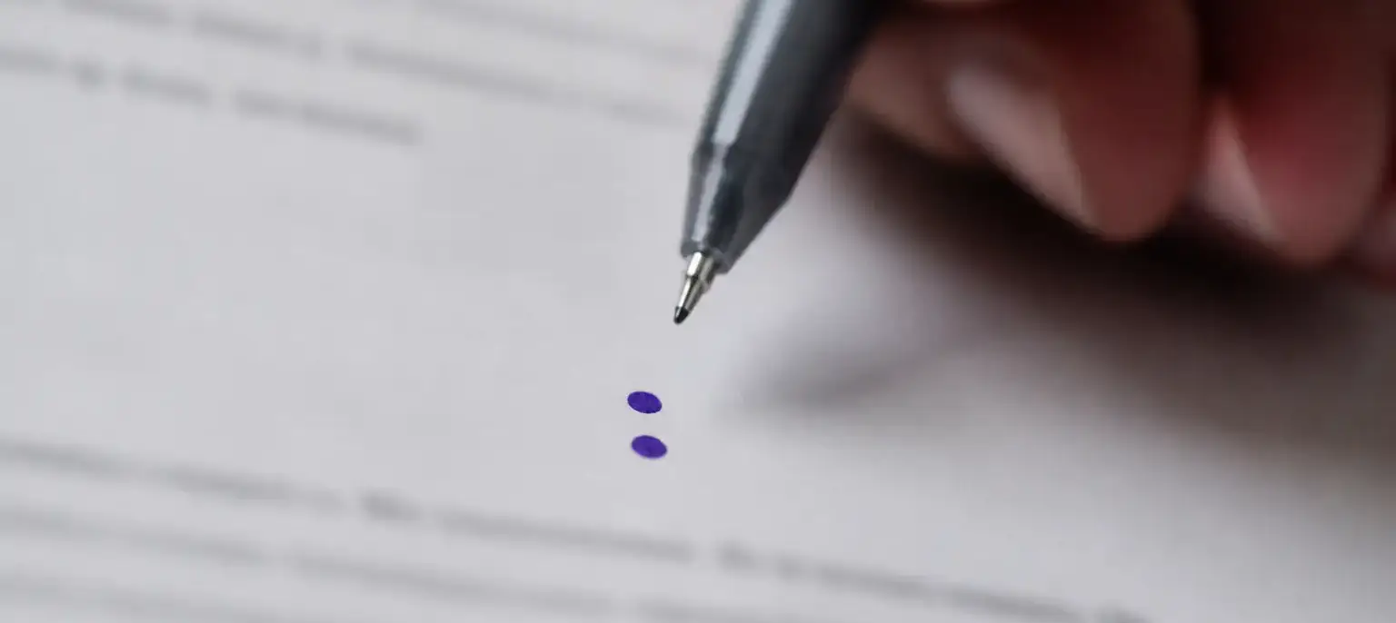 Deux points superposés tracés à l’encre violette sur une feuille blanche, entre deux lignes de texte