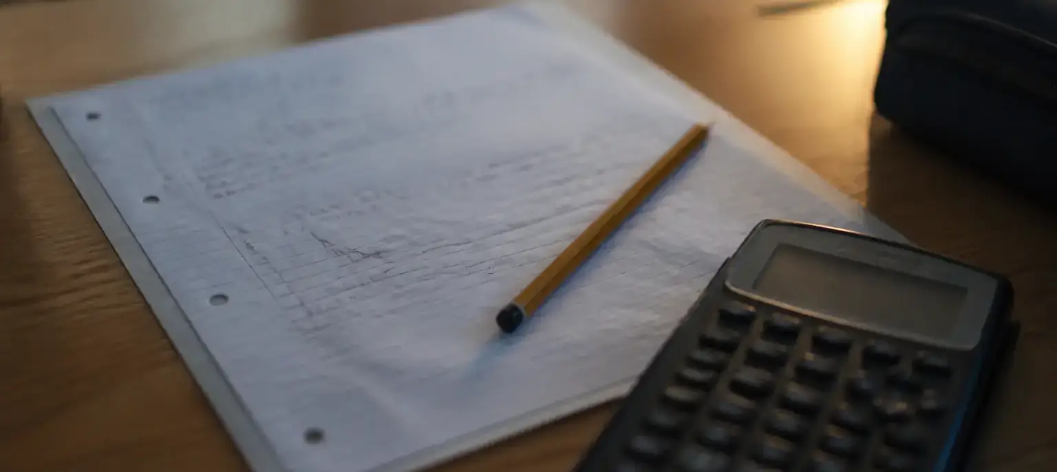 Un bulletin scolaire flou, une calculatrice et un crayon posés sur un bureau d’élève