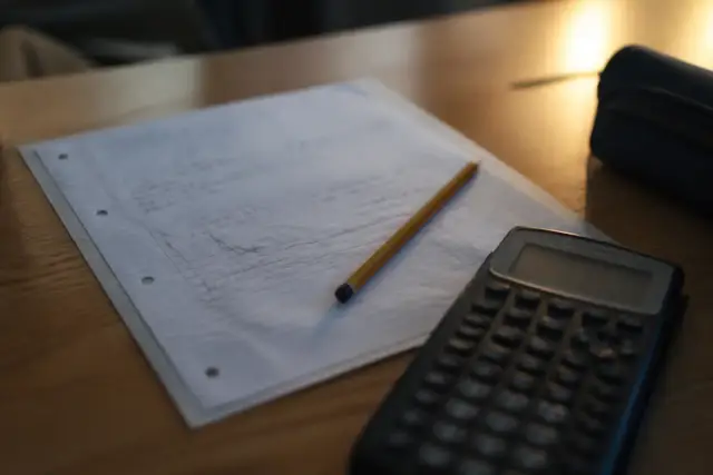 Un bulletin scolaire flou, une calculatrice et un crayon posés sur un bureau d’élève
