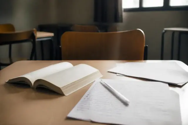 Un livre ouvert et des feuilles de notes sur une table d’examen, une chaise vide en face