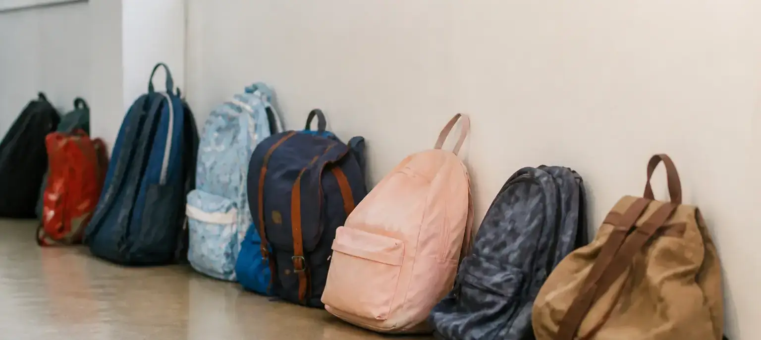Une rangée de cartables d’enfants de tailles différentes posés contre un mur de couloir d’école