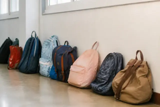 Une rangée de cartables d’enfants de tailles différentes posés contre un mur de couloir d’école