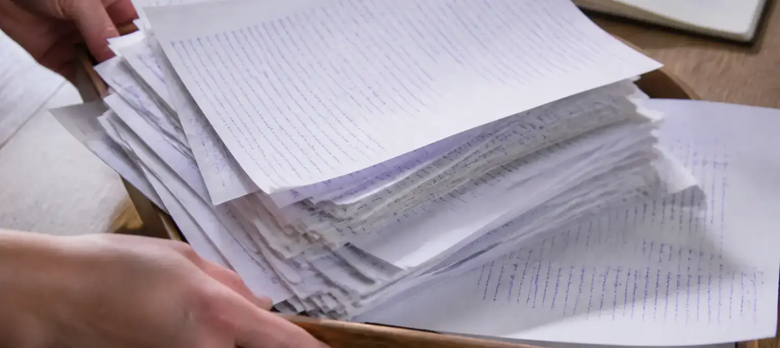 Une pile de feuilles annotées à l’encre violette, débordant d’un plateau de bois