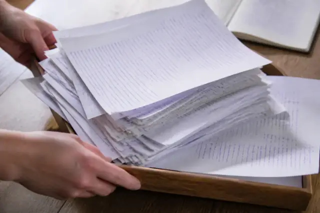 Une pile de feuilles annotées à l’encre violette, débordant d’un plateau de bois