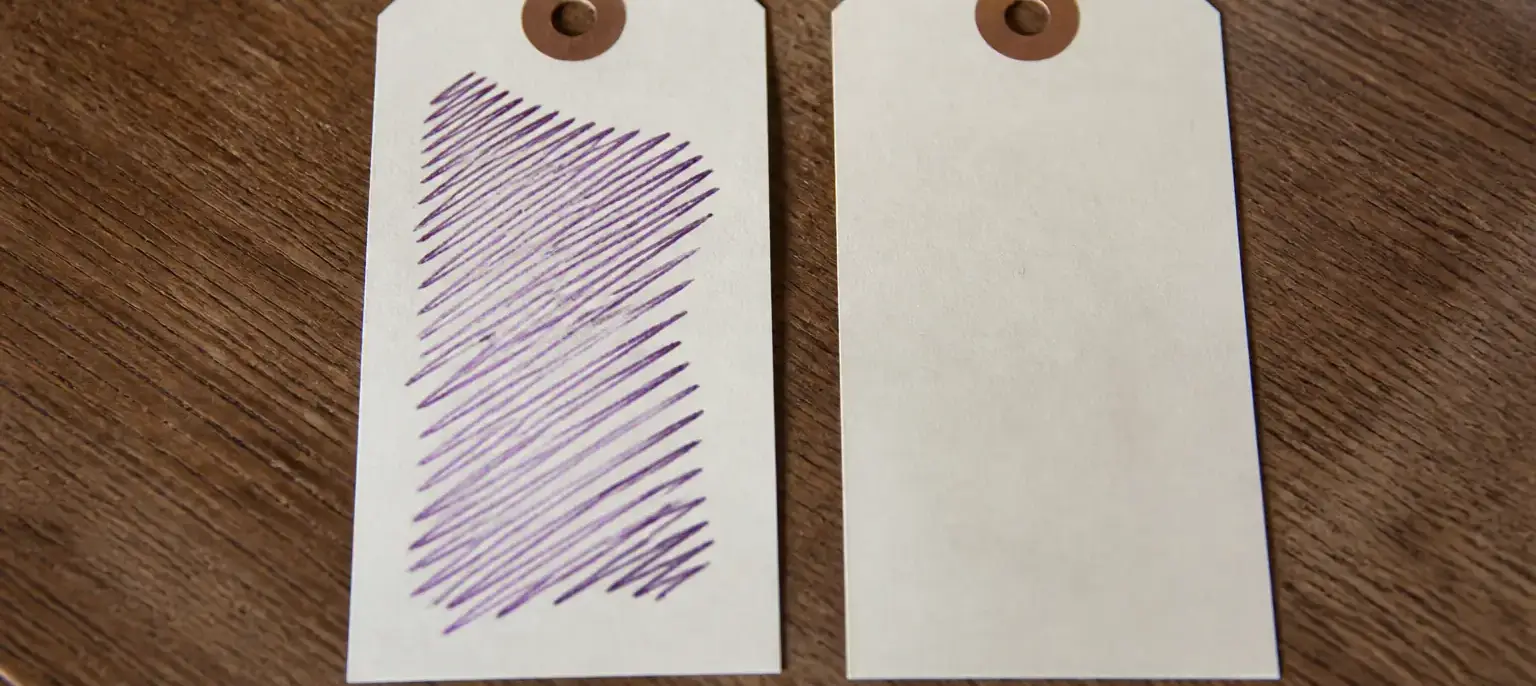 Deux étiquettes de papier identiques posées côte à côte, l’une annotée à l’encre violette
