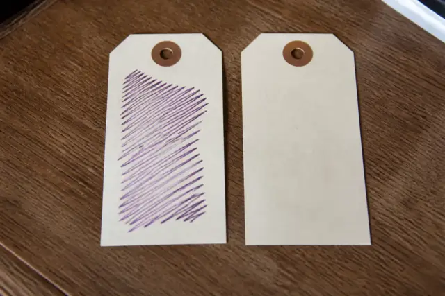 Deux étiquettes de papier identiques posées côte à côte, l’une annotée à l’encre violette