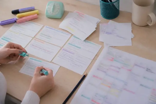Fiches de révision en bristol étalées sur un bureau clair, surligneurs pastel, minuteur de cuisine et planning papier