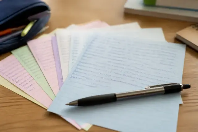 Des fiches bristol de couleurs pâles étalées en éventail sur un bureau, un stylo posé dessus