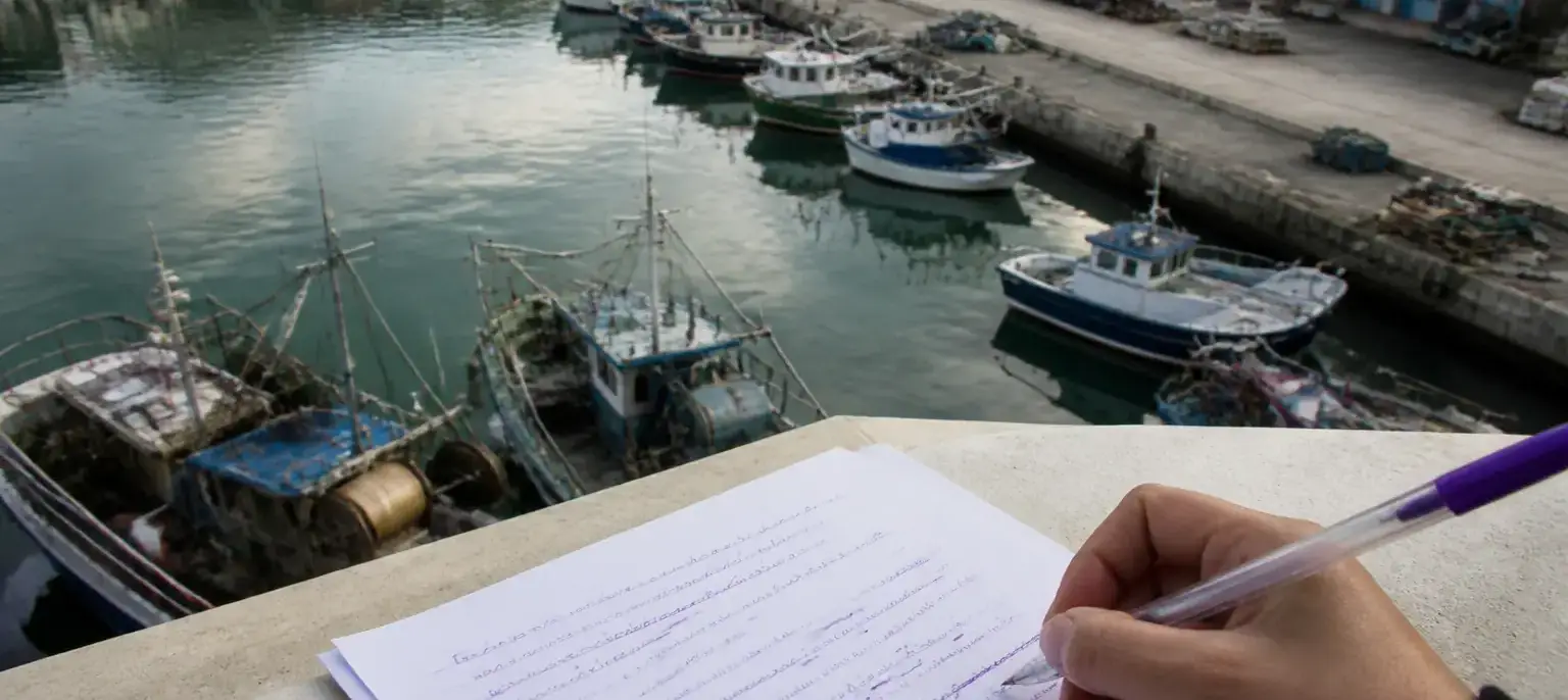 Un port aux bateaux de pêche vu de haut, une feuille annotée à l’encre violette au premier plan