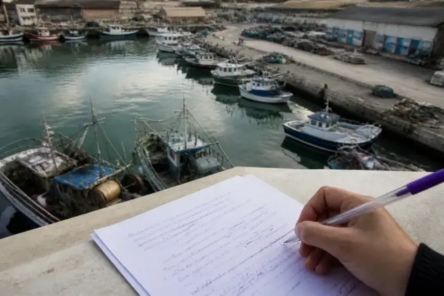 Un port aux bateaux de pêche vu de haut, une feuille annotée à l’encre violette au premier plan