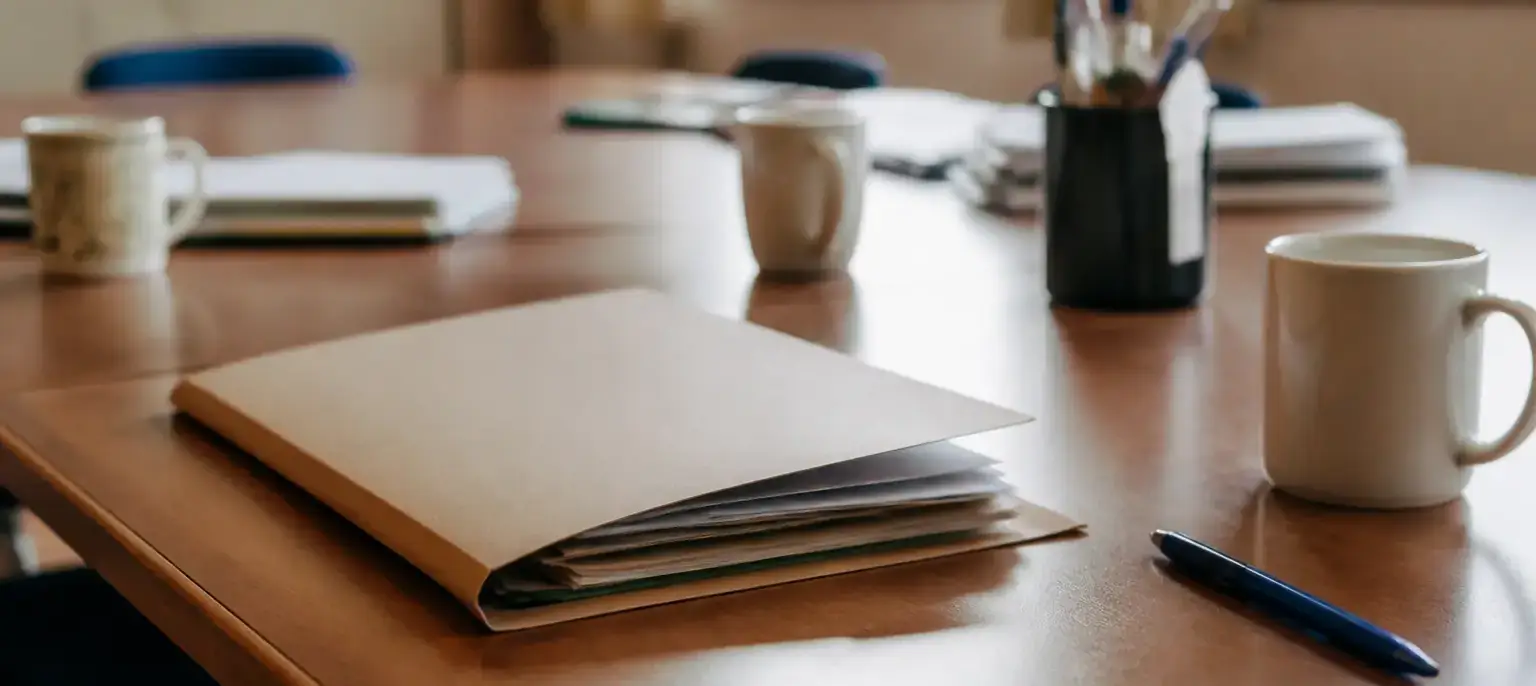 Un dossier cartonné entrouvert et quelques feuillets posés sur un bureau de salle des professeurs