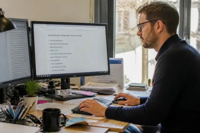 Personne travaillant sur ordinateur, écran affichant des synonymes de "cordialement" pour emails